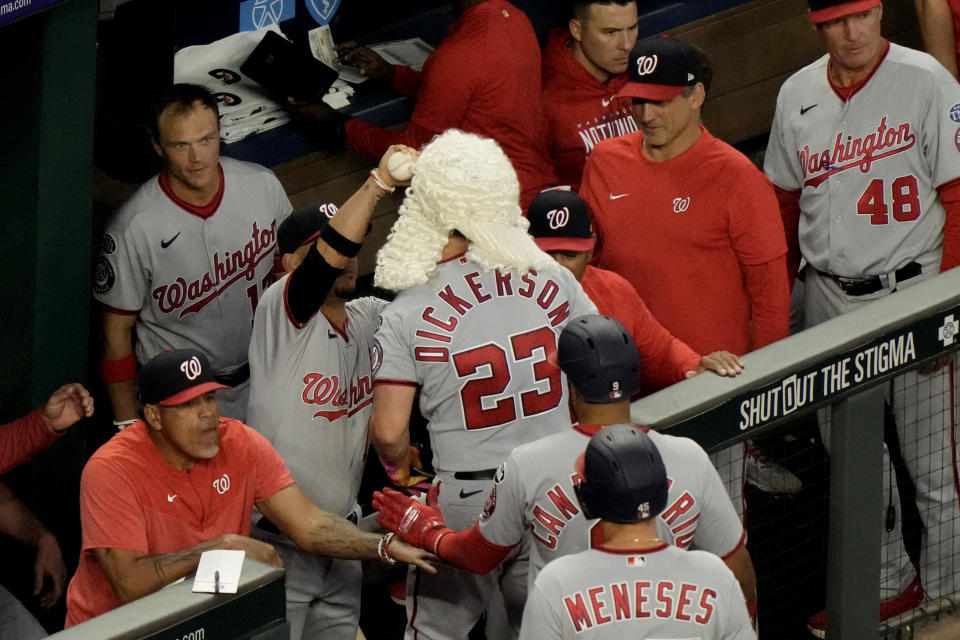Washington Nationals' Corey Dickerson (23) gets fitted with a wig as he prepares to celebrate in the dugout after hitting a three-run home run during the sixth inning of a baseball game against the Kansas City Royals Friday, May 26, 2023, in Kansas City, Mo. (AP Photo/Charlie Riedel)