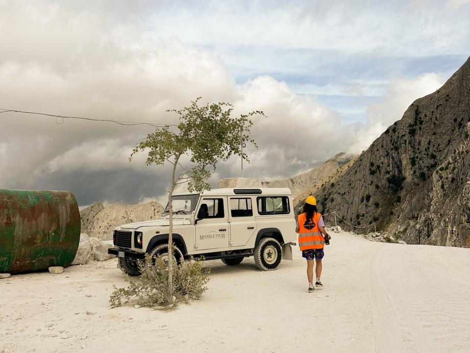 A person and a jeep on top of a mountain with clouds looming on the left