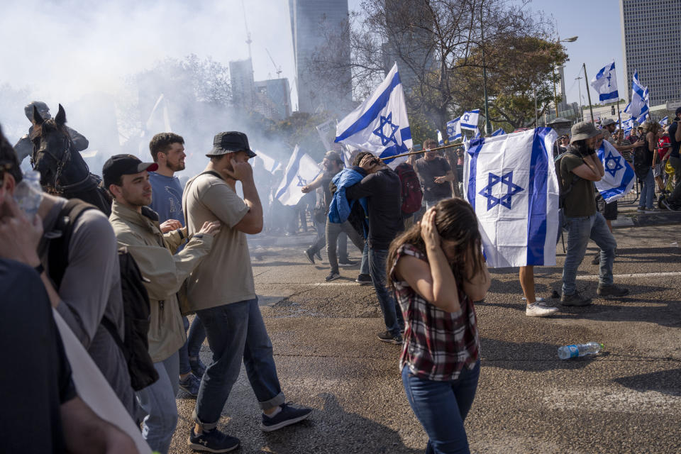 Israelis react to stun grenades fired by police to to disperse them from blocking a main road during a protest against plans by Prime Minister Benjamin Netanyahu's new government to overhaul the judicial system, in Tel Aviv, Israel, Wednesday, March 1, 2023. (AP Photo/Oded Balilty)