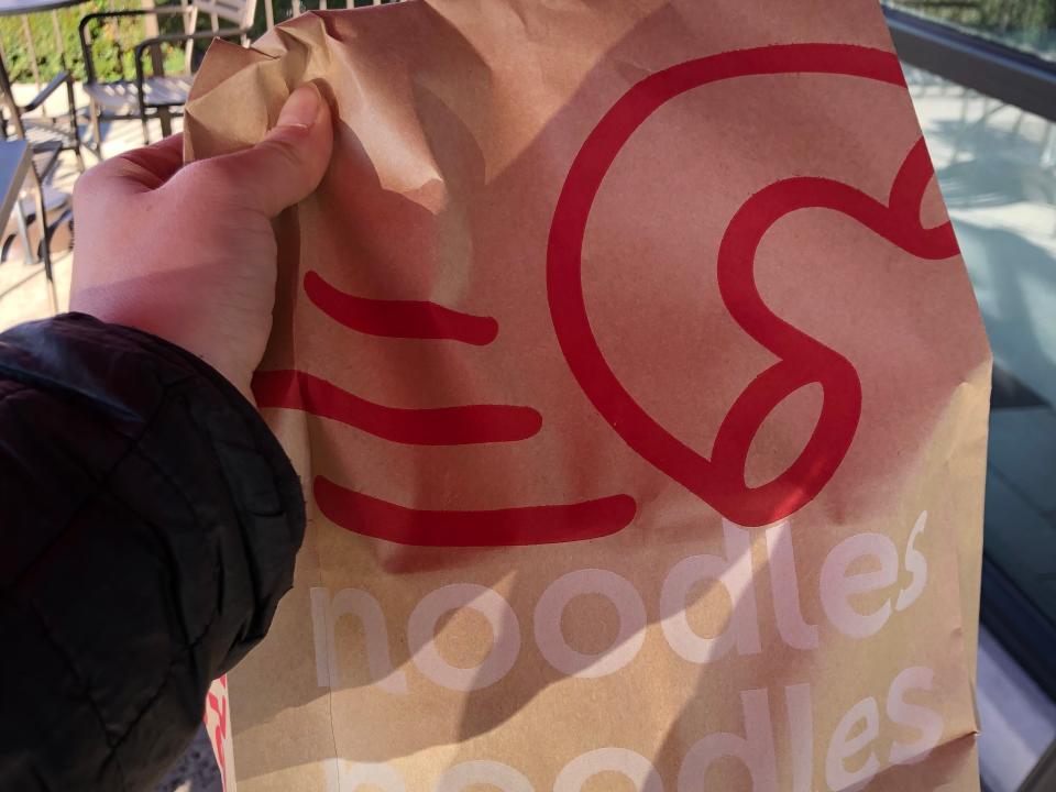 The writer holding Noodles & Company bag out