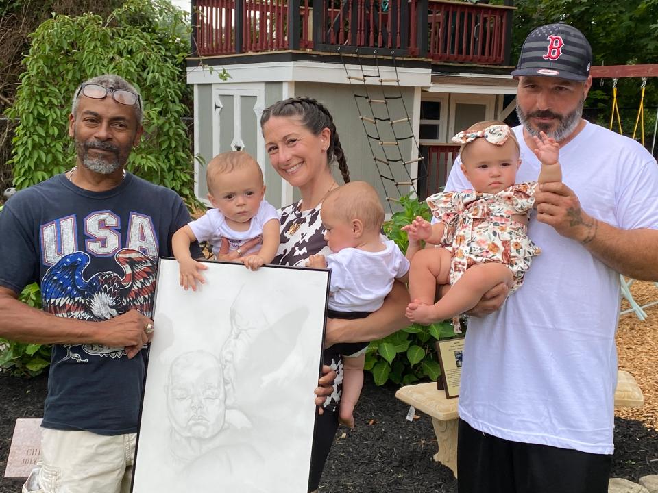 Family friend Sterling Isaac, left, holds his birthday gift to the Ness-Bettencourt family of Taunton: a sketch of mother Ashley Ness holding baby Chesley May, who died in February. Ashley and boyfriend Val Bettencourt hold their surviving quadruplets, identical twin boys Chance and Cheston and daughter Chatham, at their first birthday party on Saturday, July 29, 2023.