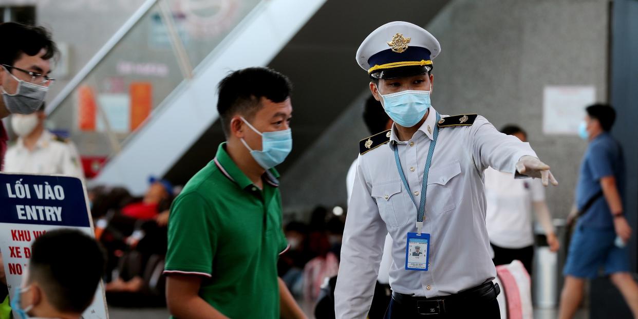 A staff member (R) from Vietnam's Centre of Disease Control assists passengers wearing face masks as they queue up for temperature checks at the departures terminal at Danang's international airport on July 27, 2020. (Photo by Hoang Khanh / AFP) (Photo by HOANG KHANH/AFP via Getty Images)