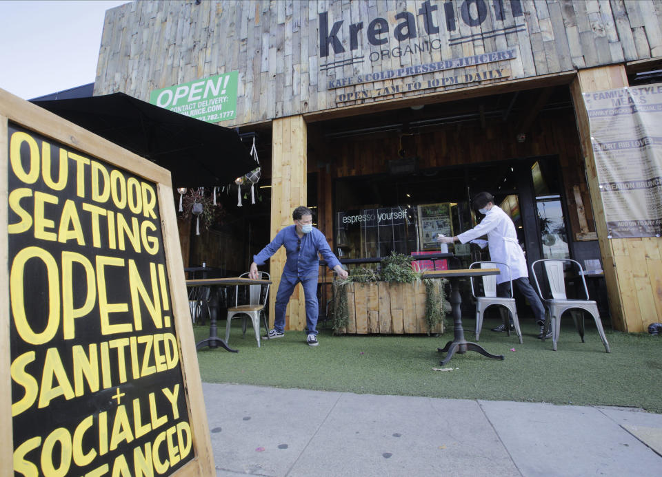 Kreation Organic manager Frank D'Andrea, left, measures a required six-feet distance between tables as his staff gets ready for customers to sit outdoors in Los Angeles, Friday, May 29, 2020. Populous Los Angeles County won approval Friday to reopen restaurants and hair-cutting businesses to customers. At the same time, remote Lassen County, the first California jurisdiction to backpedal on a reopening plan, reversed itself again and decided to allow in-person dining and shopping in stores after determining it mitigated its first small outbreak of coronavirus cases. (AP Photo/Damian Dovarganes)