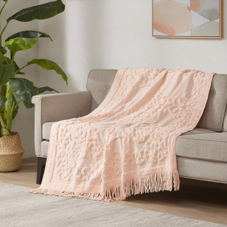 the pink tufted throw with fringe draped on a couch in a living room