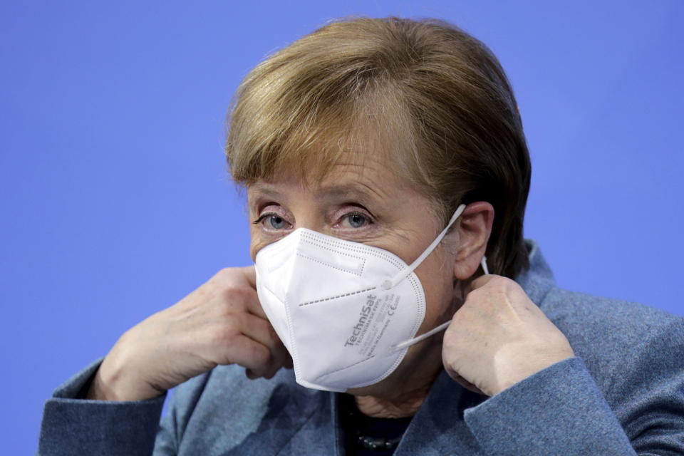 German Chancellor Angela Merkel removes her mask at the start of a news conference after meeting with vaccine producers and Germany's state prime ministers via video conference, in Berlin, Germany, Monday Feb. 1, 2021. (Hannibal Hanschke/Pool via AP)