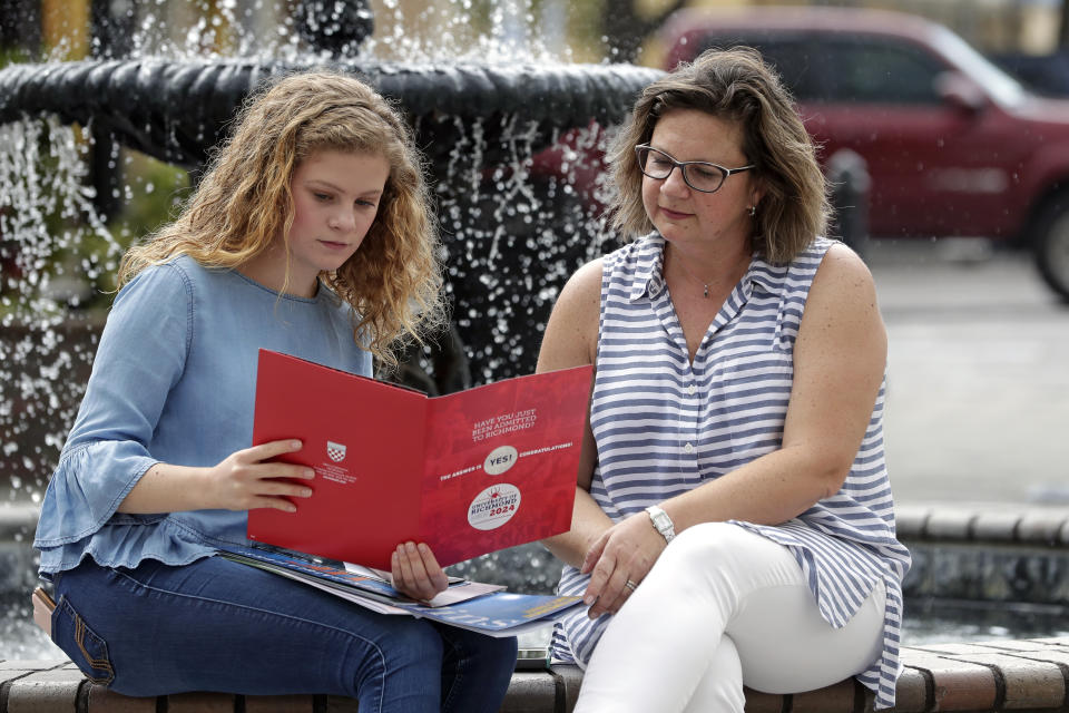 In this Friday, April 10, 2020, photo in Sanford, Fla., Serra Sowers, left, and her mother Ebru Ural look over brochures from various colleges. The coronavirus pandemic has changed the process of college visits to online and virtual interviews. (AP Photo/John Raoux)