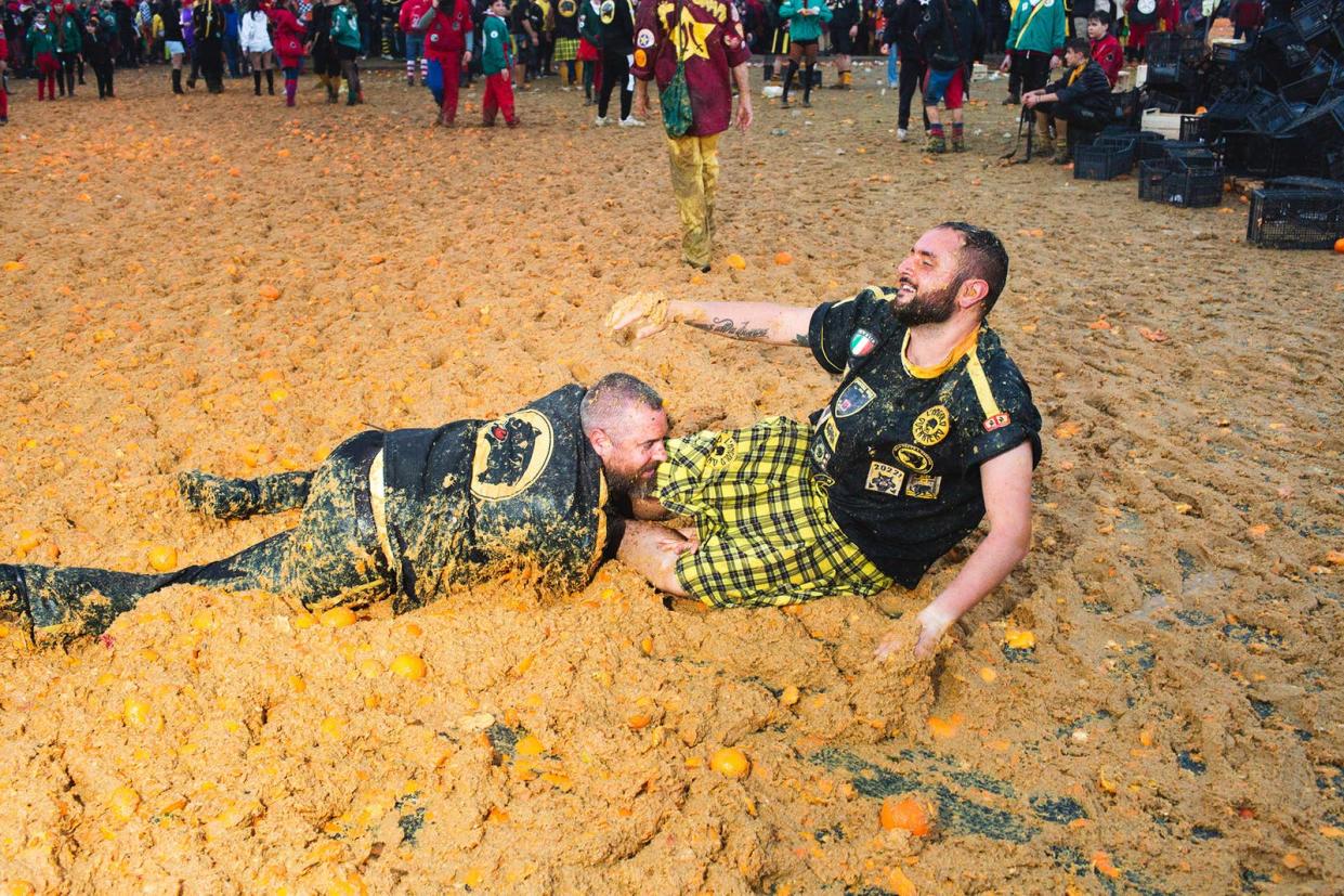 The ground outside is covered in inches of what looks like mud, a brown-orange pulp from crushed oranges obliterated into carnage. A bearded man lying down in the pulp leans onto a smiling bearded man wearing a kilt
