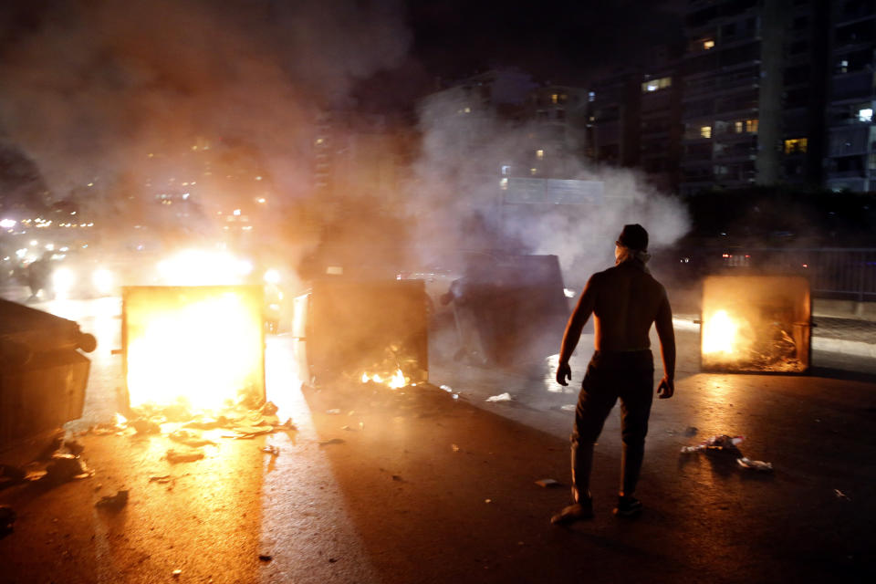 A supporter of Lebanese Prime Minister Saad Hariri burns garbage containers to block a main road, in Beirut, Lebanon, Tuesday, Oct. 29, 2019. Hariri resigned Tuesday, bowing to one of the central demands of anti-government demonstrators shortly after baton-wielding Hezbollah supporters rampaged through the main protest camp in Beirut, torching tents, smashing plastic chairs and chasing away protesters. (AP Photo/Bilal Hussein)