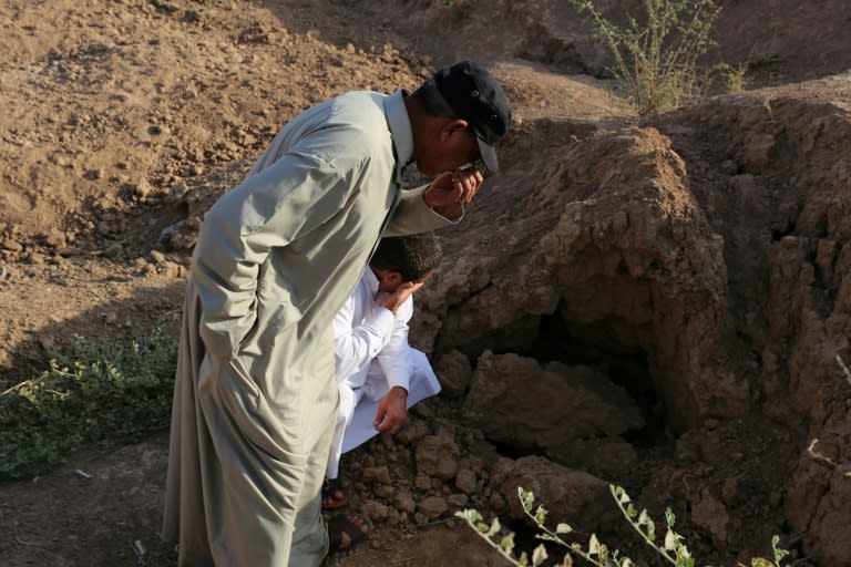Iraqi men pinch their nose as they inspect the site of a pit containing the bodies of Islamic State (IS) group fighters in the Iraqi town of Dhuluiyah, north of Baghdad