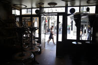 People walk past a closed cafe where chairs and tables are stacked up, in Paris, Monday, June 1, 2020. Local Parisians are savoring their cafe au lait and croissants at the Left Bank's famed Cafe de Flore, or on the cobbled streets of the ancient Le Marais for the first time in almost three months. As virus confinement measures were relaxed Tuesday, cafes around France were allowed to reopen. (AP Photo/Thibault Camus)