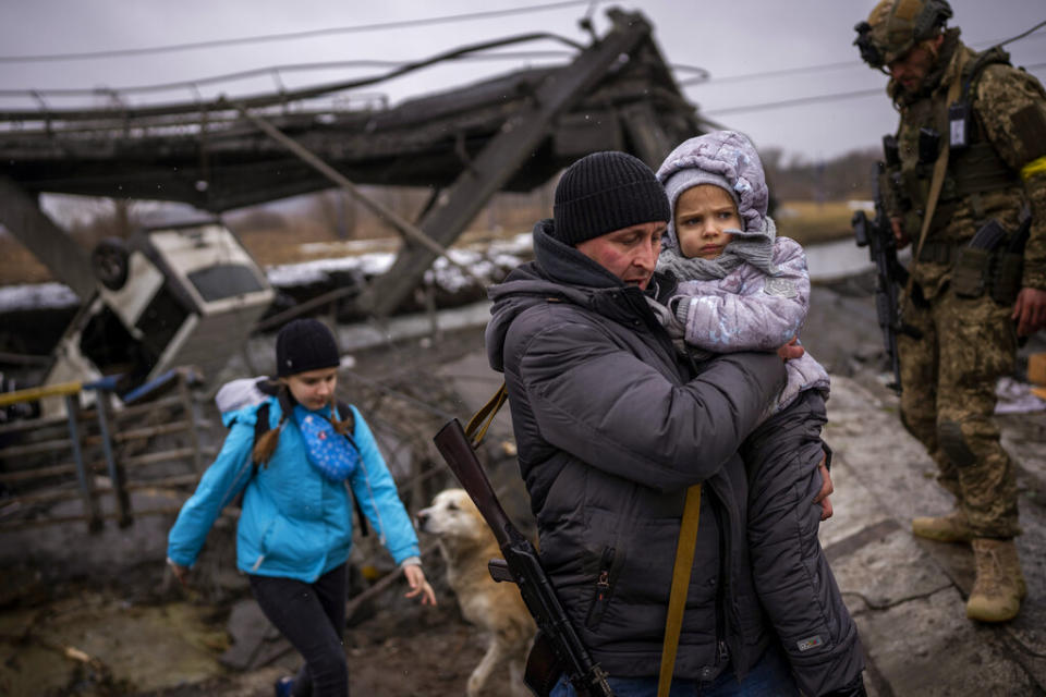 Local militiaman Valery, 37, carries a child as he helps a fleeing family across a bridge destroyed by artillery on the outskirts of Kyiv, Ukraine, Wednesday. Russian forces have escalated their attacks on crowded cities in what Ukraine's leader called a blatant campaign of terror. (AP Photo/Emilio Morenatti)
