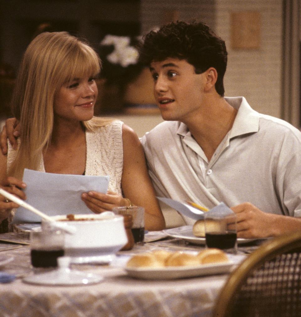 Kirk Cameron sitting at a table with his arm around Julie McCullough on the set of "Growing Pains"