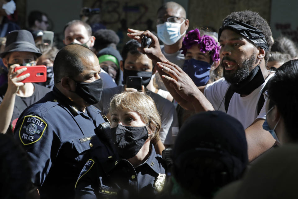 A protester, right, who did not give his name talks with Seattle Police assistant chiefs Adrian Diaz, left, and Deanna Nollette, center, Thursday, June 11, 2020, inside what is being called the "Capitol Hill Autonomous Zone" in Seattle. The officers were attempting to walk to the police department's East Precinct building, which has been boarded up and abandoned except for a few officers inside, but the protester, in a move that angered some other protesters, said he would walk with the officers to a side entrance of the precinct rather than have them walk directly through a crowd of angry protesters. Following days of violent confrontations with protesters, police in Seattle have largely withdrawn from the neighborhood, where protesters have created a festival-like scene. (AP Photo/Ted S. Warren)