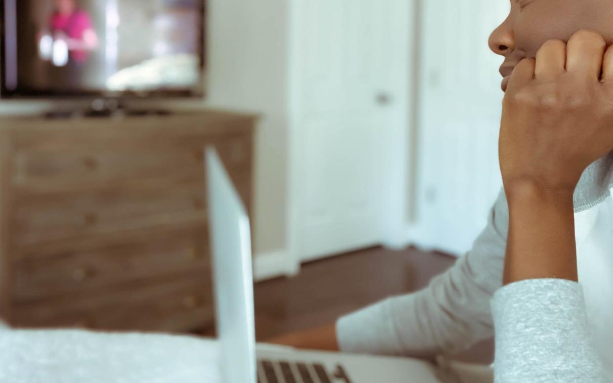 Close-up of mid adult woman watching tv in bed while working on laptop