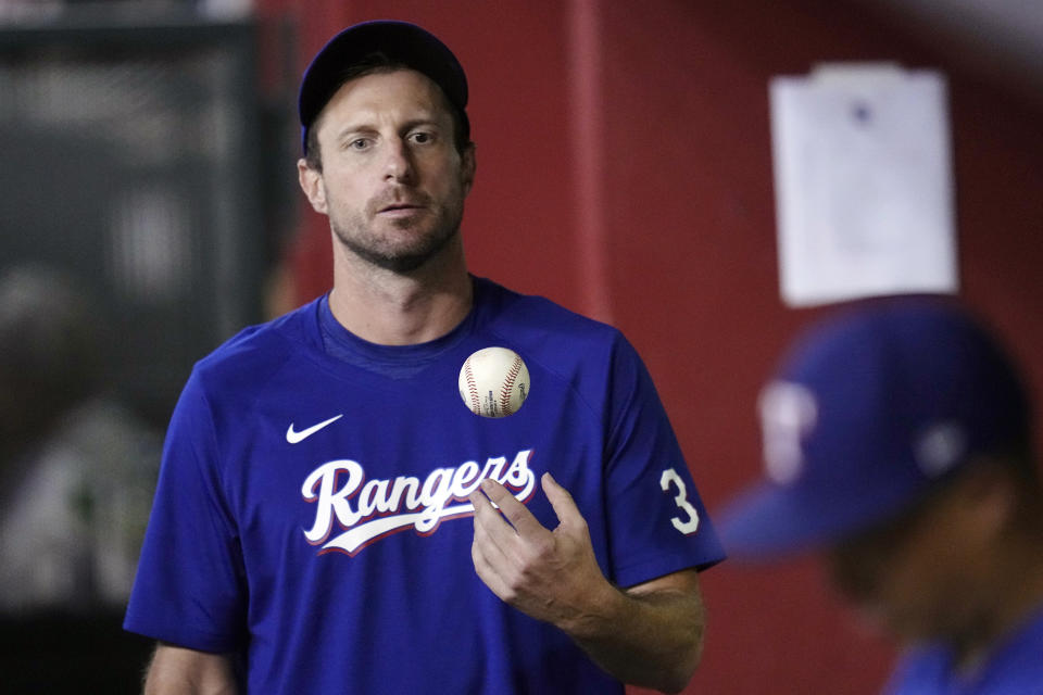 FILE- Texas Rangers' Max Scherzer flips the ball in the air as he paces the dugout during the seventh inning of a baseball game against the Arizona Diamondbacks Tuesday, Aug. 22, 2023, in Phoenix. Scherzer logged at least 179 innings in 10 of his first 16 years in the majors. And the three-time Cy Young Award winner learned some tough lessons on the road to pitching deep into games. That's one reason why the Rangers right-hander thinks Major League Baseball needs to look a lot deeper than a roster limit if it wants to return starting pitching to prominence. (AP Photo/Ross D. Franklin, File)