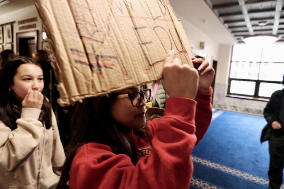 A student carrying a "Red for Ed" sign walks through the State Capitol in support of increased education funding for Alaska's public schools. (Photo by Claire Stremple/Alaska Beacon)