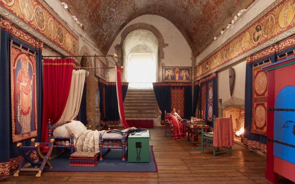 A four-poster bed and tapestries hang on the walls of the large stone-walled room