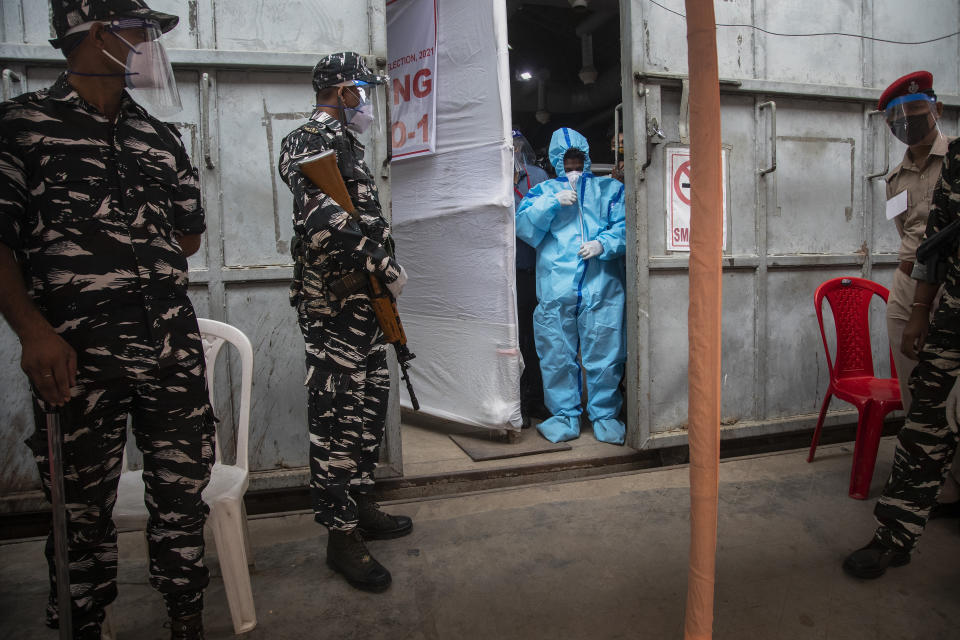 A counting agent in protective suit stands as security men guard during the counting of votes of Assam state assembly election in Gauhati, India, Sunday, May 2, 2021. With Indian hospitals struggling to secure a steady supply of oxygen, and more COVID-19 patients dying amid the shortages, a court in New Delhi said it would start punishing government officials for failing to deliver the life-saving items. (AP Photo/Anupam Nath)