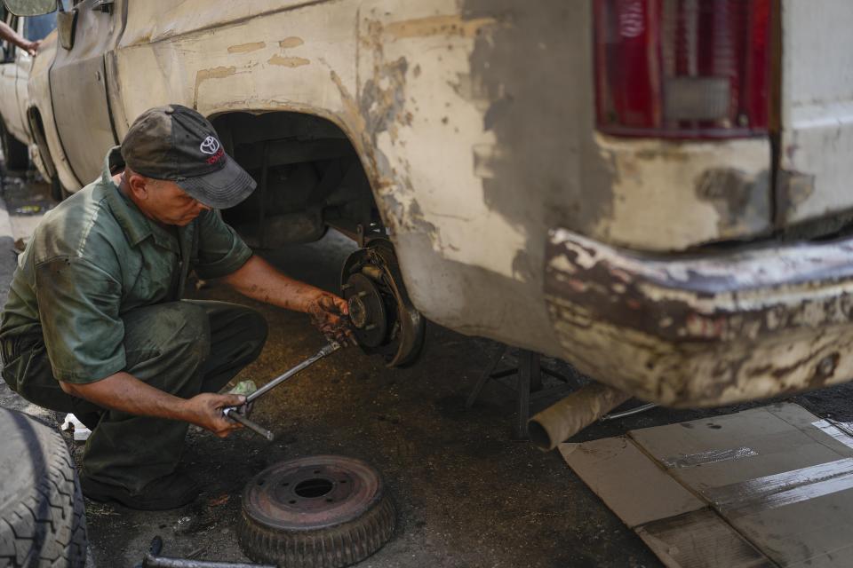 Ramon Arellano repairs the brakes of a customer's car on a street of the Catia neighborhood in Caracas, Venezuela, Wednesday, April 20, 2022. Mechanics are increasingly busy as they try to coax a little more life out of aging vehicles in a country whose new car market collapsed and where few can afford to trade up for a better used one. (AP Photo/Matias Delacroix)