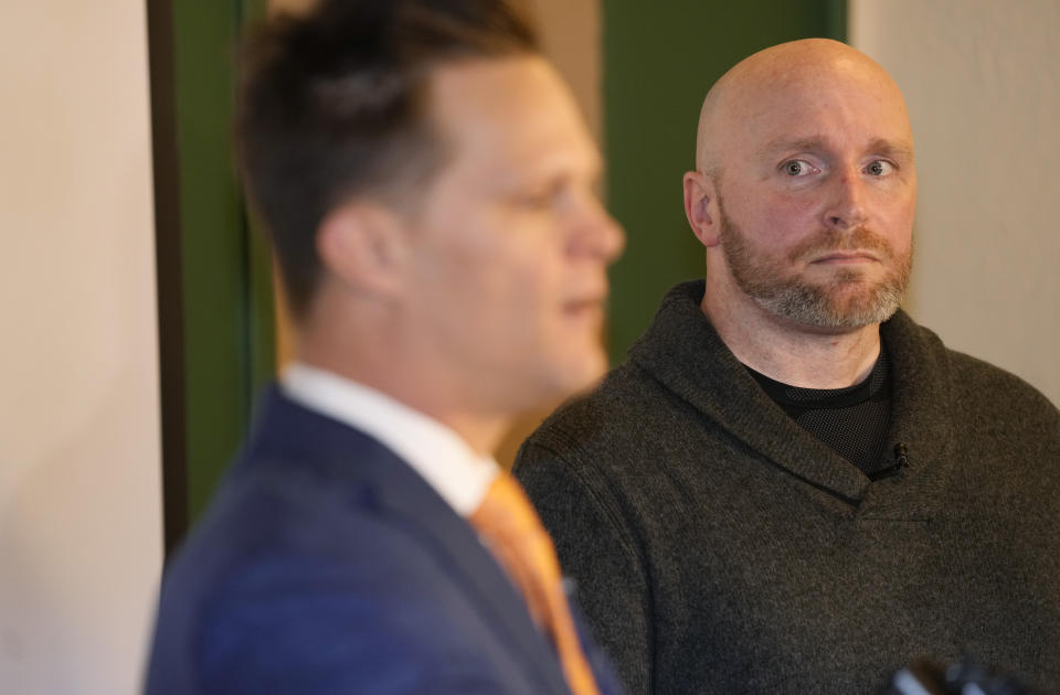 Scott Verti, back, looks on as his attorney, Kurt Zaner, responds to questions during a news conference ast the Denver Press Club on Thursday, Jan. 19, 2023, in Denver. Verti, who says he was repeatedly sexually abused as a teenager by a Catholic priest while serving as an altar boy in a parish in Fort Collins, Colo., is suing that defrocked priest and the Archdiocese of Denver. (AP Photo/David Zalubowski)