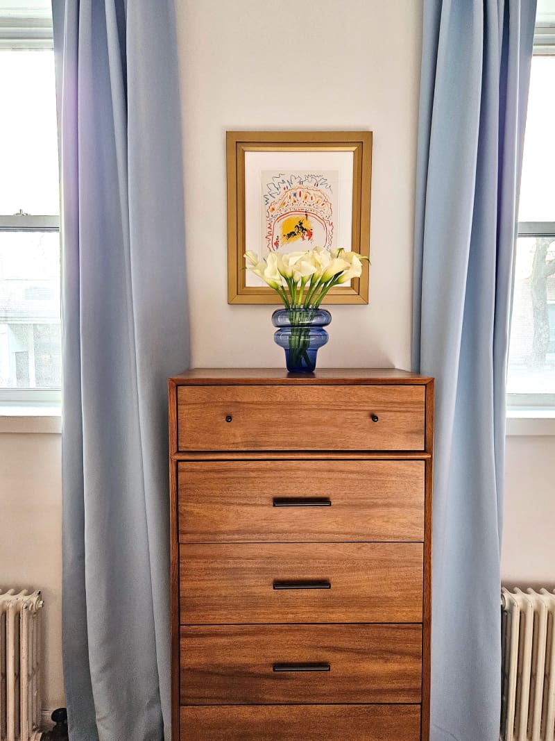 wood dresser between 2 windows with light blue curtains