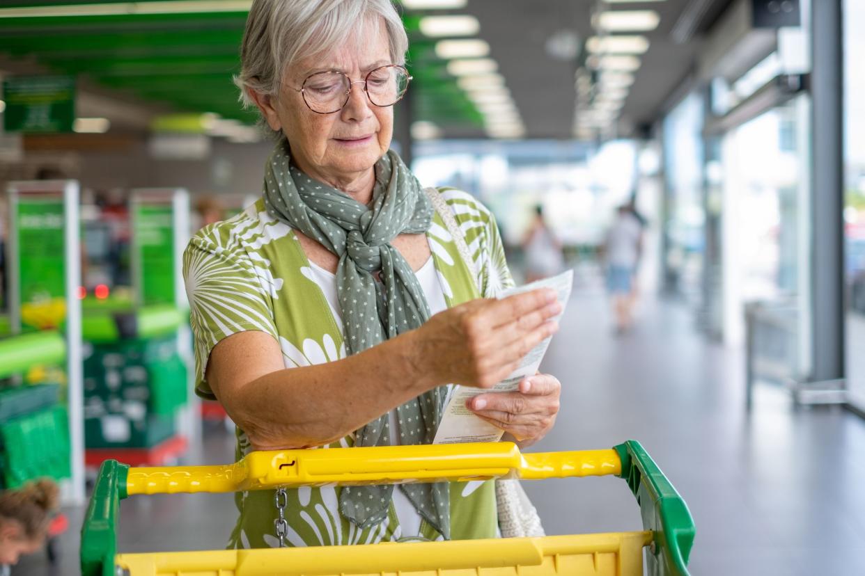 Senior woman in the supermarket checks her grocery receipt looking worried about rising costs - consumerism concept, rising prices, inflation