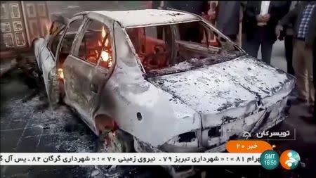 People stand near a burning car in Tuyserkan, Hamadan Province, Iran, December 31, 2017 in this still image taken from video. IRINN/ReutersTV via REUTERS