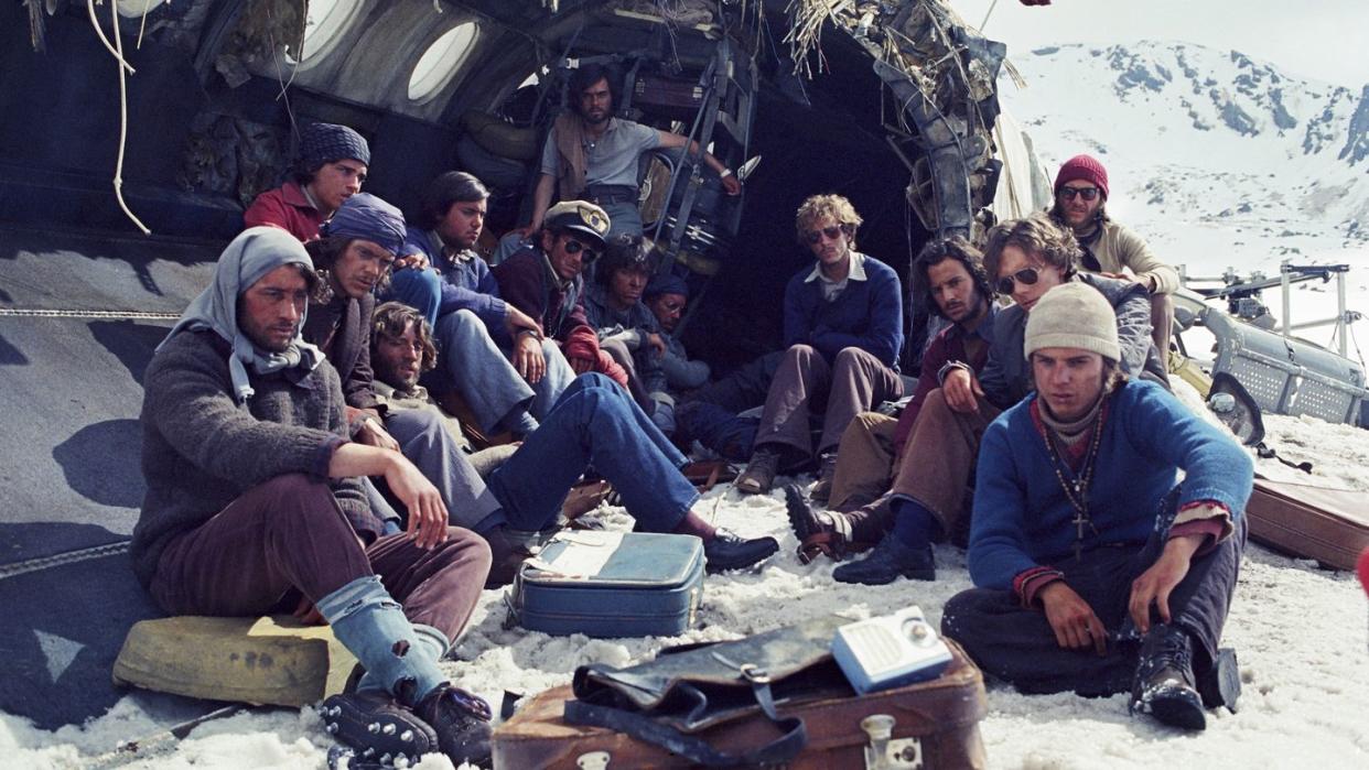 a scene from the movie society of the snow with survivors sitting near a wrecked airplane