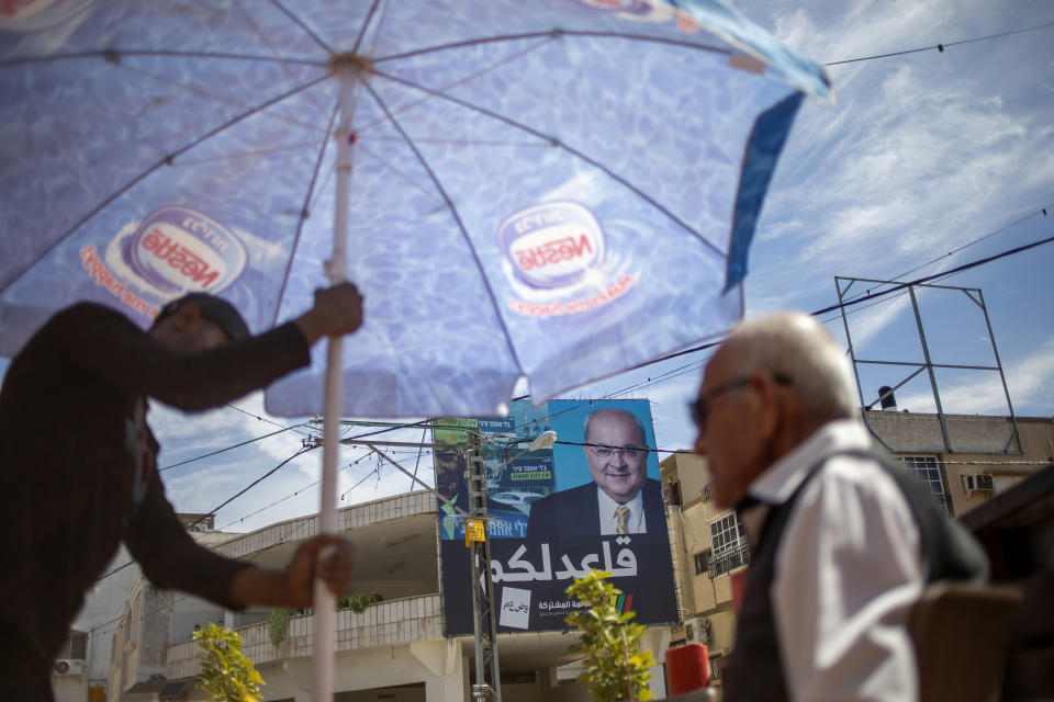 In this Thursday, March 5, 2020 photo, Israeli Arabs in a coffee shop near an election campaign poster showing Israeli Politician Ahmad Tibi of the Joint List in Tira, Israel. A surge in Arab voter turnout was key to depriving Prime Minister Benjamin Netanyahu and his nationalist allies of a parliamentary majority in this week’s Israeli election. Undercutting Netanyahu’s ambitions was celebrated as sweet payback in the nearly 2 million-strong minority that the hard-line leader had relentlessly tried to tarnish as disloyal to the state. The Arabic reads, "I sit with you." (AP Photo/Ariel Schalit)