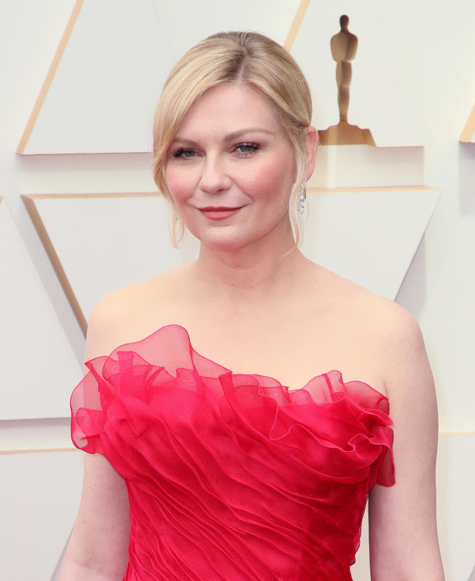 Kirsten wearing a taffeta style red strapless dress. Her blonde hair is tied back and she is smiling