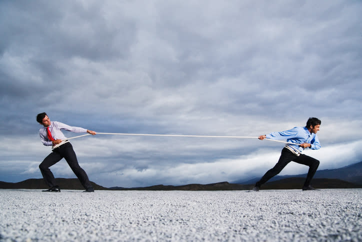 Two businessmen engaged in a game of tug of war.