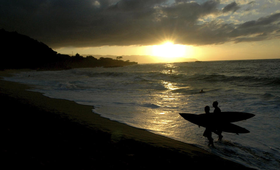 FILE - Participants in the In Memory of Eddie Aikau walk out of the ocean at sunset after the opening ceremony in Waimea Bay near Haleiwa, Hawaii, on Nov. 30, 2006. One of the world's most prestigious and storied surfing contests is expected to be held on Sunday, Jan. 22, 2023, in Hawaii for the first time in seven years - if conditions are right. And female surfers will be competing alongside the men for the first time in the 39-year history of The Eddie Aikau Big Wave Invitational. (AP Photo/Lucy Pemoni, File)