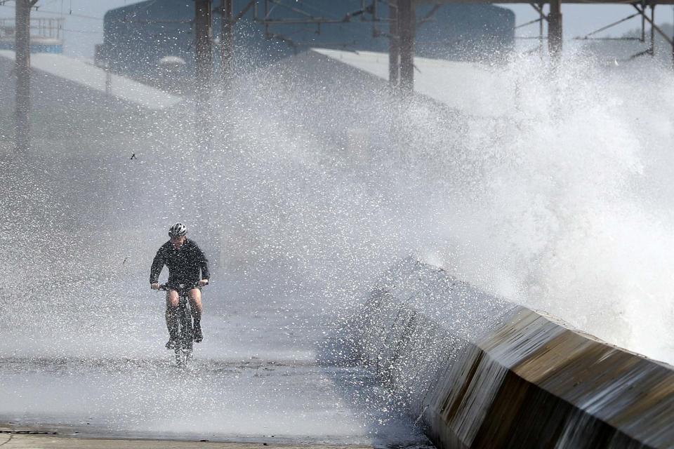 A cyclist is hit by a wave as he cycles along the shoreline in Saltcoats on the west coast of North Ayrshire as gusts of up to 70mph could hit coastal areas: PA