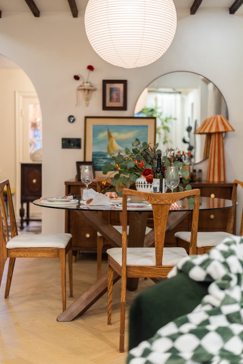 A glass and wood dining table surrounded by wooden chairs with white cushions.