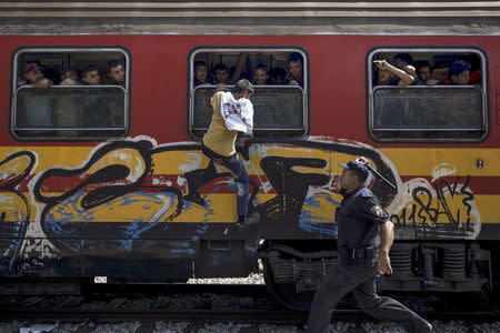 A policeman tries to stop a migrant from boarding a train through a window at Gevgelija train station in Macedonia, close to the border with Greece, August 15, 2015. REUTERS/Stoyan Nenov