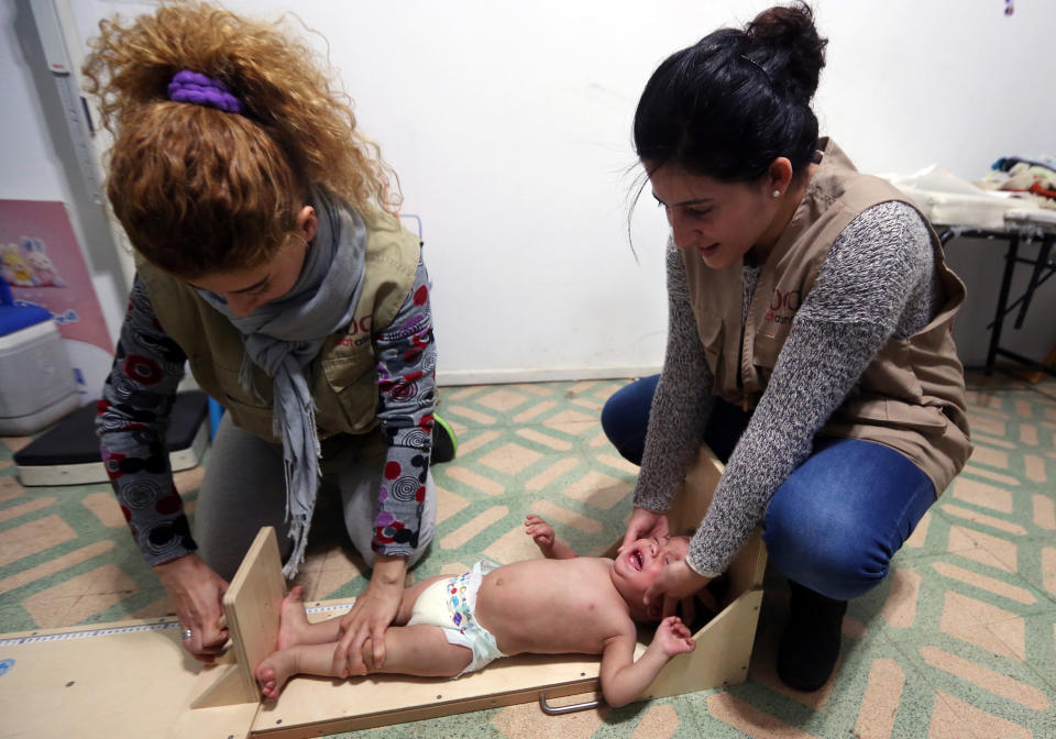 In this Tuesday, March 11, 2014 photo, two aid workers measure one year-old Syrian refugee Jawad al-Abbas at a medical clinic in the town of Kab Elias in Lebanon's Bekaa Valley. Three years after Syria’s uprising began to overthrow President Bashar Assad, spiraling into a war that has killed over 140,000 people and sending over 2.5 million people fleeing into neighboring countries, aid workers say are now seeing malnutrition emerge, once a barely known scourge in Syrian society. (AP Photo/Bilal Hussein)