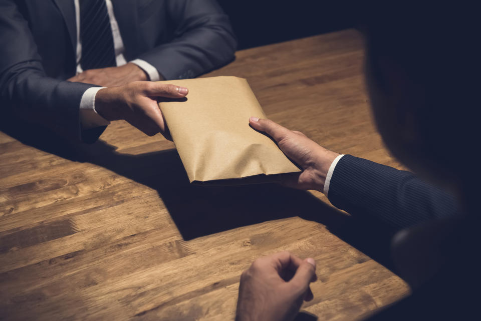 Businessman giving money in the envelope to his partner in the dark - bribery and venality concept