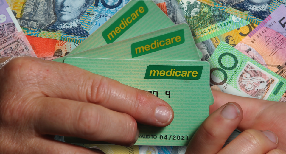 Two people holding a Medicare card with Aussie money behind 