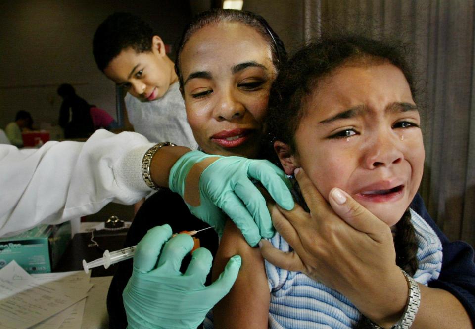 Maya Daniel, 4, sheds tears as she anticipates a flu shot given by LPN Cisily Harris at the Lentz Public Health Clinic on Dec. 9, 2003. Maya was being comforted by her mother Joan Daniel and watched by her older brother Mark Daniel, 9. Metro Health spokesman Brian Todd said that the clinic administered 1,150 flu shots on this day, more than doubling the 500 given out the day before.