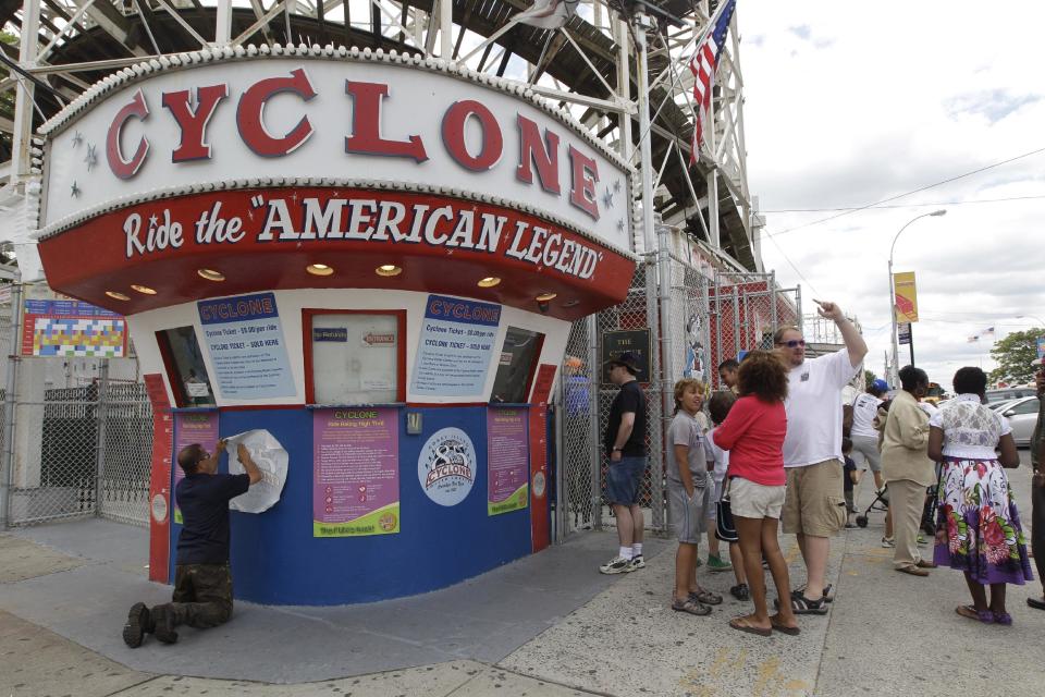 In a Tuesday, June 26, 2012 photo taken on Coney Island in New York,  a maintenance worker applies a decal commemorating the Cyclone's 85th anniversary while people wait in line to buy tickets. The New York City landmark and international amusement icon will be feted Saturday, June 30 with a birthday party in its honor.   (AP Photo/Mary Altaffer)