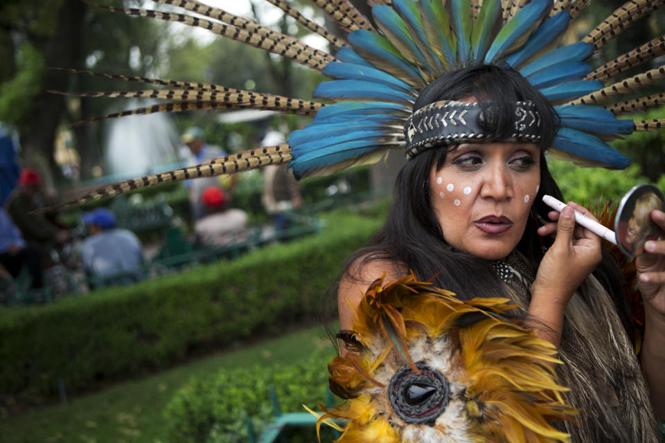 Street performer Judit Pozos puts the finishing touches on her Aztec costume, as she and her partner prepare to perform blessings with incense and a conch shell, in the central square in Xochimilco, on the southern edge of Mexico City, Wednesday, May 7, 2014. In Xochimilco, busy markets stand side by side with colonial churches, and children ride to school in boats pushed by poles, along a network of canals and floating gardens that date to pre-hispanic times. The popular tourist destination was declared a UNESCO world heritage site in 1987. (AP Photo/Rebecca Blackwell)