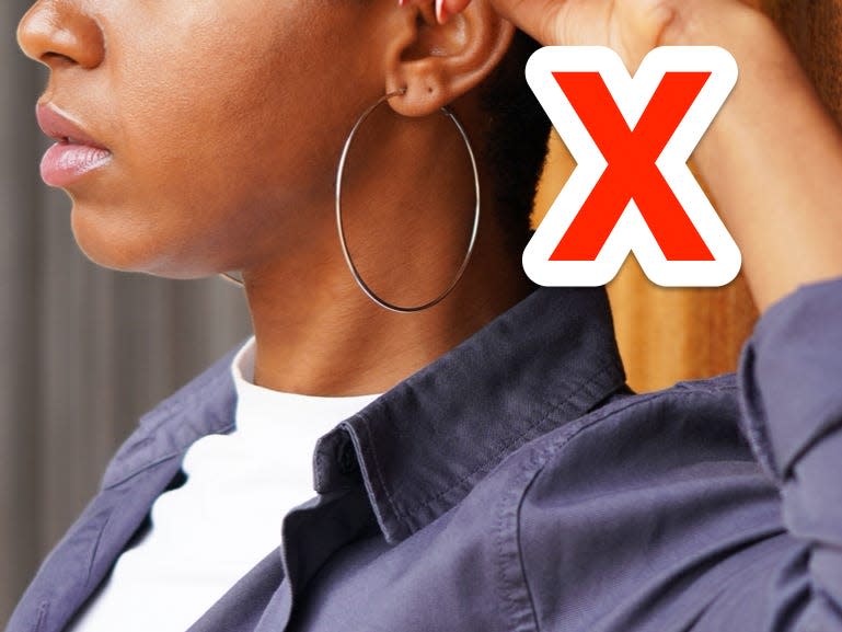 red x on top of person leaning against a wall wearing plain silver hoop earrings