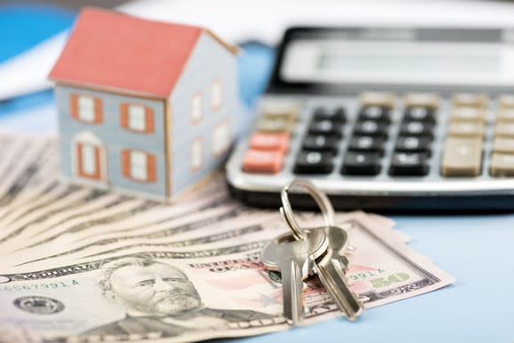 House keys on top of money next to miniature house and calculator.