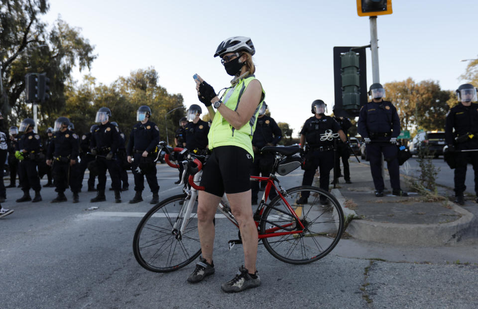 A bicyclist checks her cellphone in front of California Highway Patrol officers during a protest of the killing of George Floyd near the entrance of Highway 101 at Broadway and Woodside Road in Redwood City, Calif., on Tuesday, June 2, 2020. (Nhat V. Meyer/Digital First Media/The Mercury News via Getty Images)