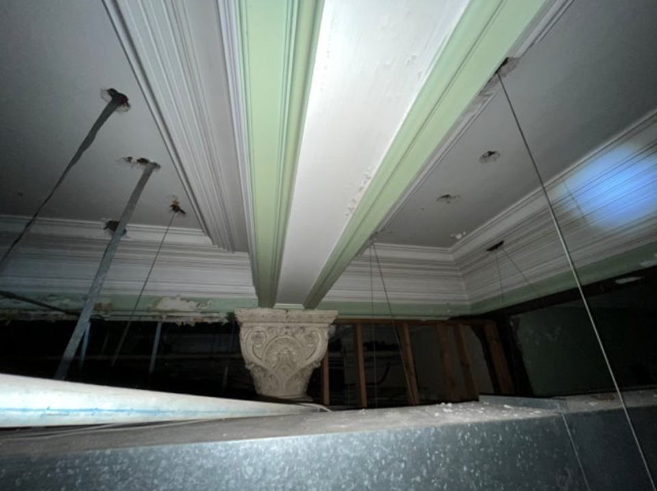 A photo taken during the initial assessment of Historic City Hall shows taller ceilings with crown molding and columns above the existing drop ceiling.