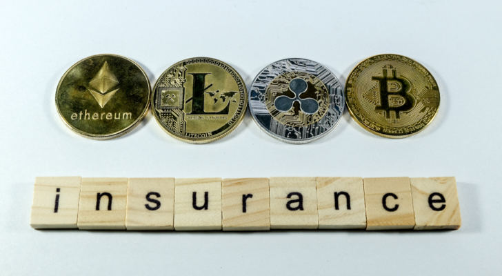 A photo pf physical representations of cryptocoins above wooden tiles bearing black letters that spell out insurance.