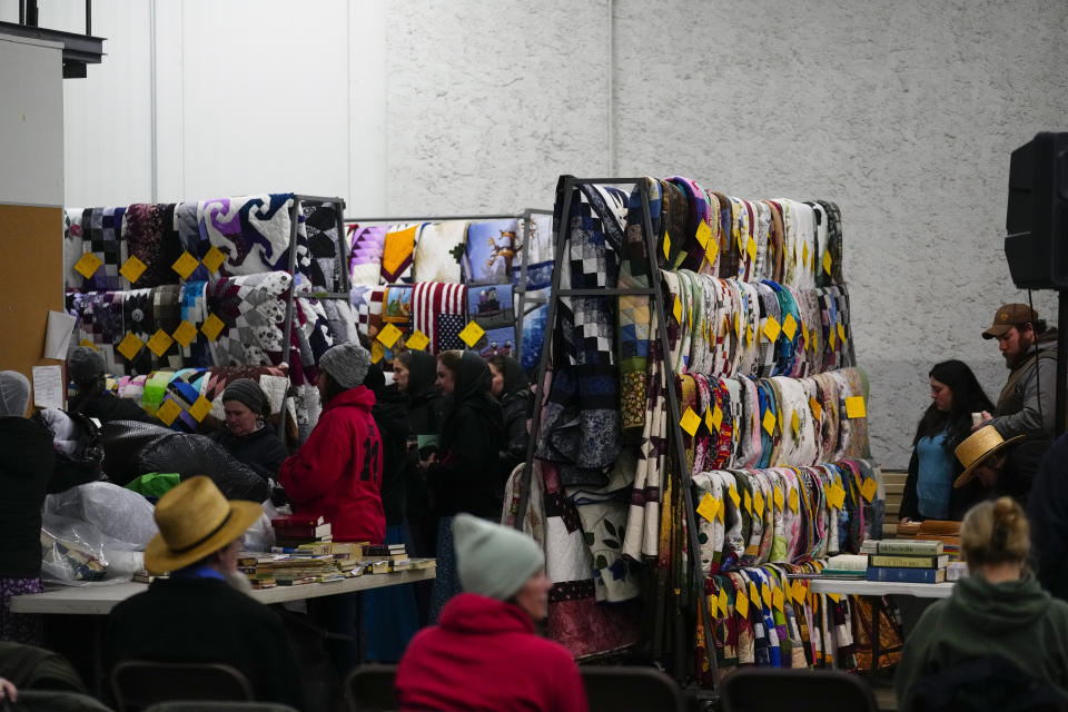 Attendees inspect quilts that will go up for auction during the 56th annual mud sale to benefit the local fire department in Gordonville, Pa., Saturday, March 9, 2024. Mud sales are a relatively new tradition in the heart of Pennsylvania's Amish country, going back about 60 years and held in early spring as the ground begins to thaw but it's too early for much farm work. (AP Photo/Matt Rourke)