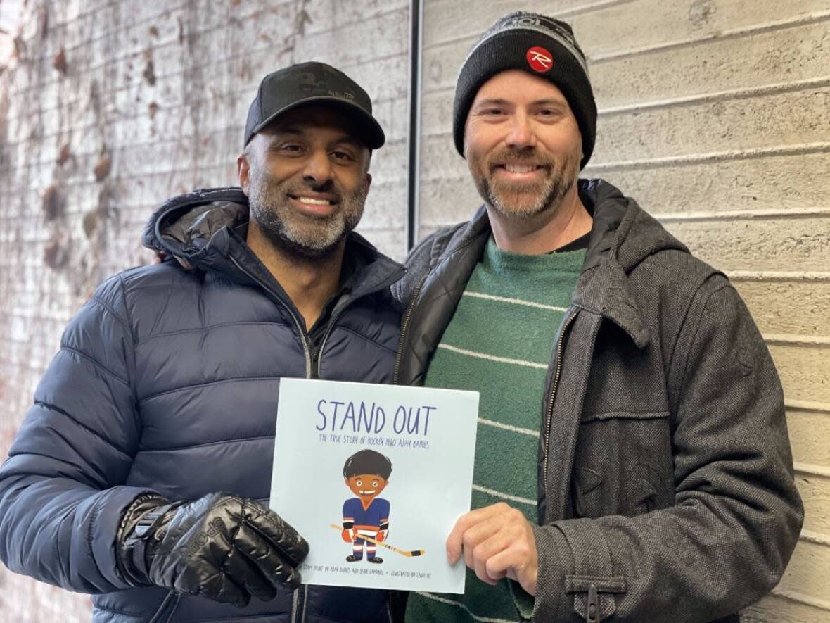 Co-authors Ajay Baines, left, and Sean Campbell hold a copy of Stand Out:The True Story of Hockey Hero Ajay Baines. (Jenifer Norwell/CBC - image credit)