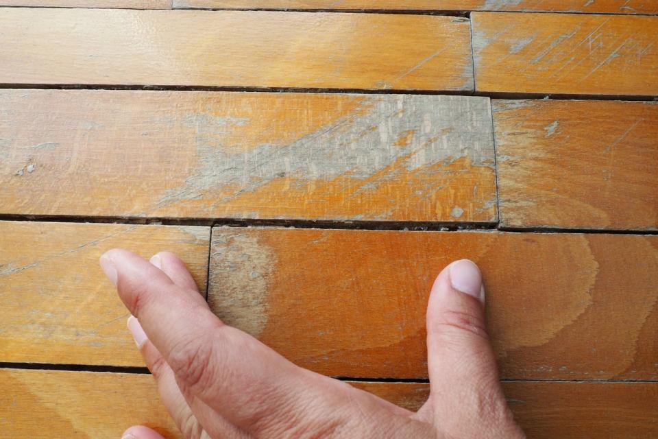 A close up of a hand feeling a hardwood floor plank.