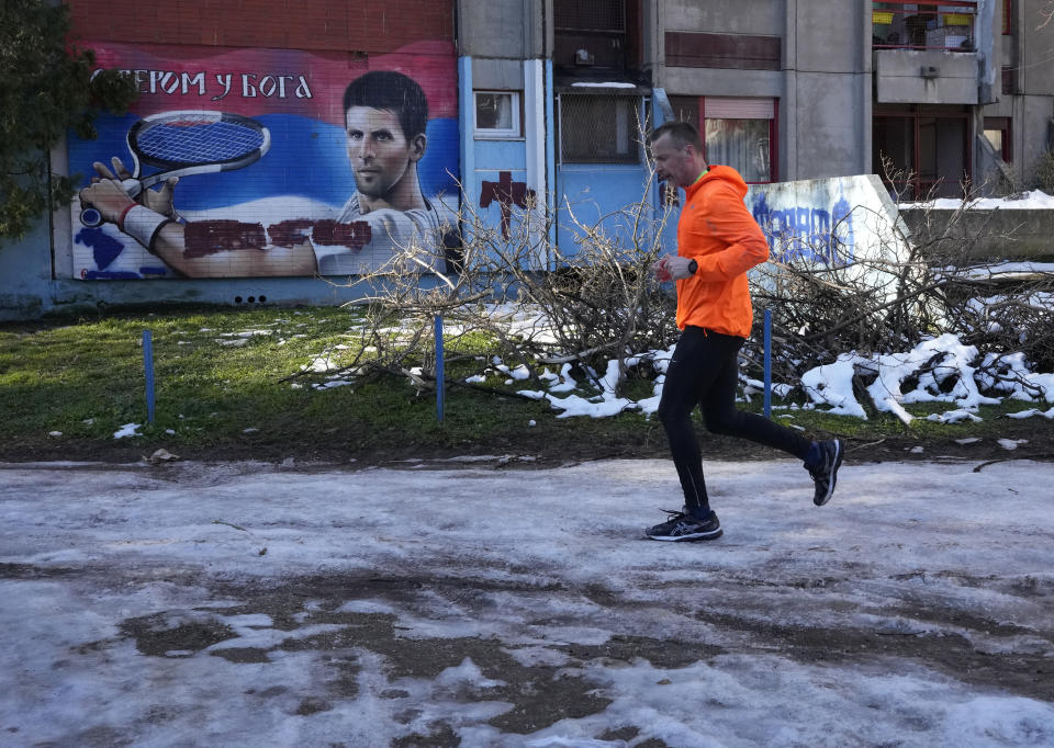 A man runs past a mural depicting Serbian tennis player Novak Djokovic, reading: "With faith in God" on a wall in Belgrade, Serbia, Sunday, Jan. 16, 2022. Novak Djokovic was preparing to leave Australia on Sunday evening after losing his final bid to avoid deportation and play in the Australian Open despite being unvaccinated for COVID-19. A court earlier unanimously dismissed the No. 1-ranked tennis player's challenge to cancel his visa. (AP Photo/Darko Vojinovic)